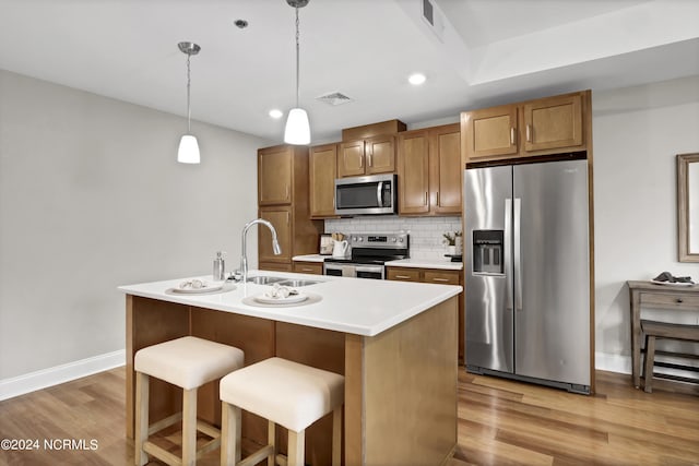 kitchen featuring brown cabinets, wood finished floors, a sink, stainless steel appliances, and backsplash