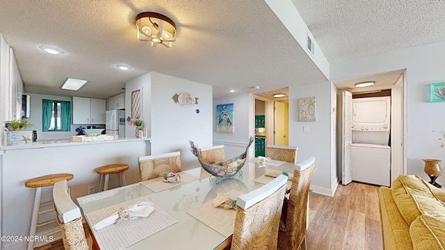 dining room with light wood-type flooring, stacked washer / dryer, and a textured ceiling