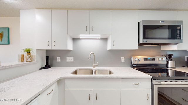 kitchen with white cabinets, appliances with stainless steel finishes, light stone counters, and sink