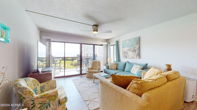 living room featuring light wood-type flooring, ceiling fan, and a textured ceiling