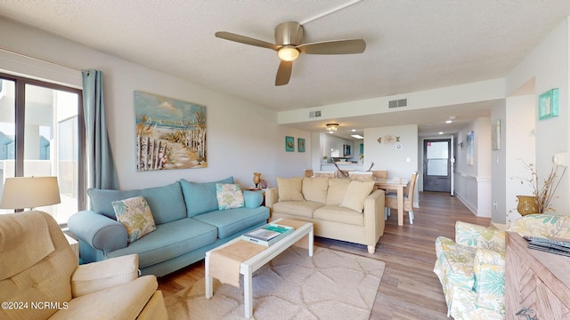 living room with a textured ceiling, light hardwood / wood-style flooring, ceiling fan, and a healthy amount of sunlight