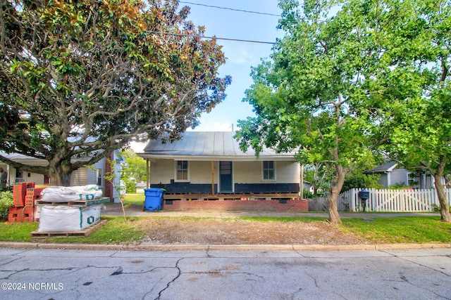 view of front of property featuring a porch, a standing seam roof, metal roof, fence, and a front lawn