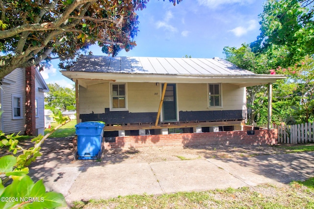 bungalow-style house featuring a standing seam roof, covered porch, metal roof, and fence