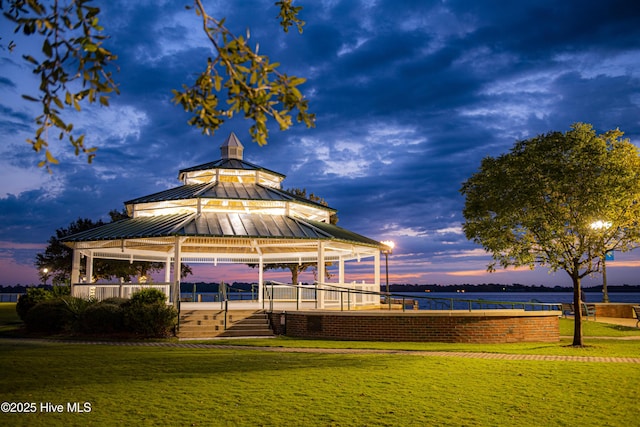 back house at dusk with a lawn, a water view, and a gazebo