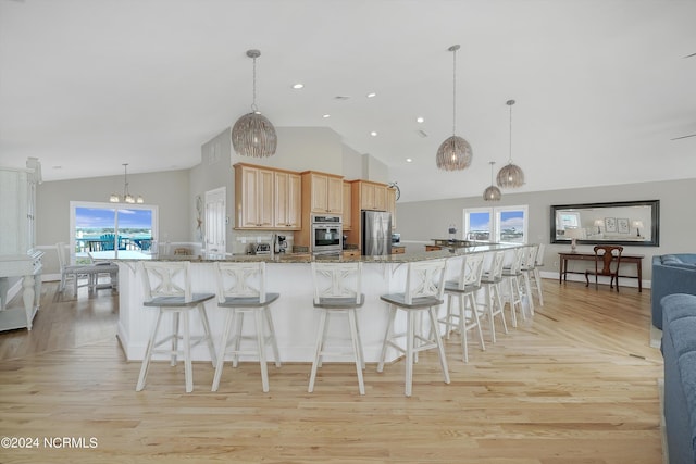 kitchen with open floor plan, stainless steel appliances, light brown cabinetry, a kitchen bar, and high vaulted ceiling