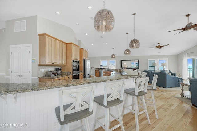 kitchen featuring a breakfast bar area, visible vents, light wood-style flooring, light brown cabinetry, and appliances with stainless steel finishes