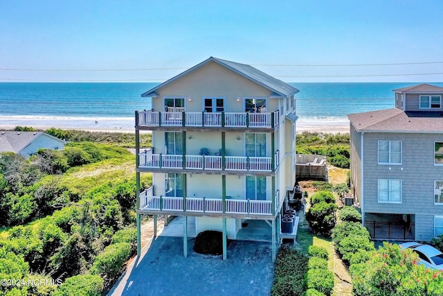 rear view of house with a balcony, a water view, and a view of the beach