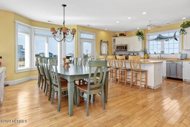 dining room with ceiling fan with notable chandelier, a wealth of natural light, sink, and light hardwood / wood-style flooring