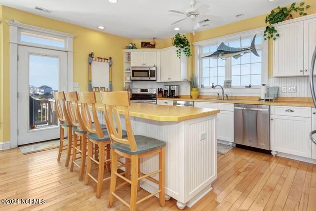 kitchen featuring light hardwood / wood-style floors, a center island, stainless steel appliances, wooden counters, and white cabinets