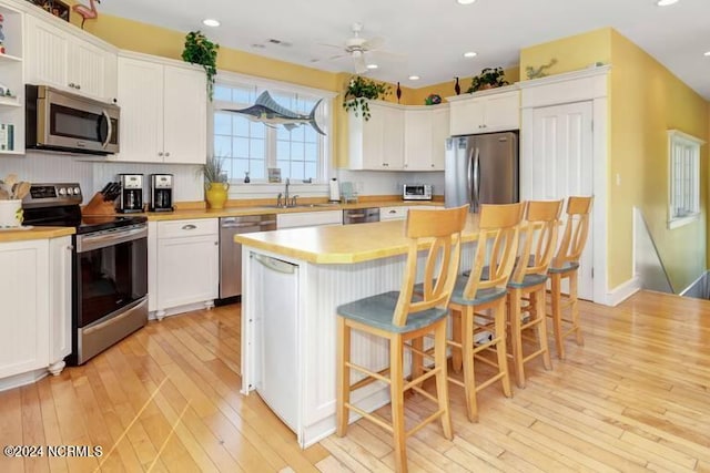 kitchen with a breakfast bar area, appliances with stainless steel finishes, a center island, ceiling fan, and light wood-type flooring