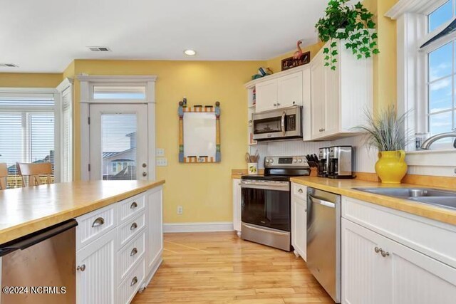 kitchen with light hardwood / wood-style flooring, appliances with stainless steel finishes, tasteful backsplash, sink, and white cabinets