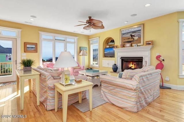 living room featuring light wood-type flooring, a lit fireplace, baseboards, and recessed lighting