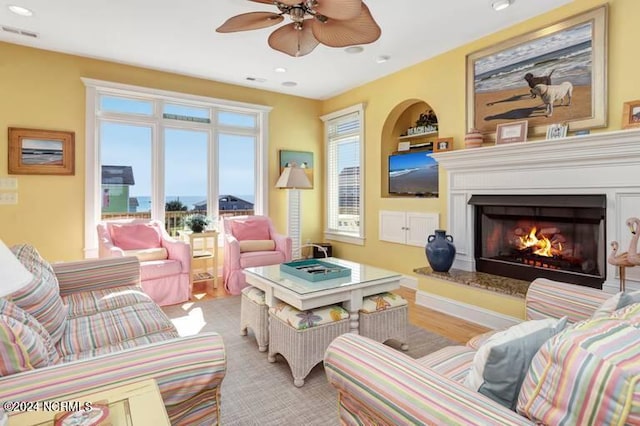 living area featuring recessed lighting, visible vents, ceiling fan, wood finished floors, and a warm lit fireplace