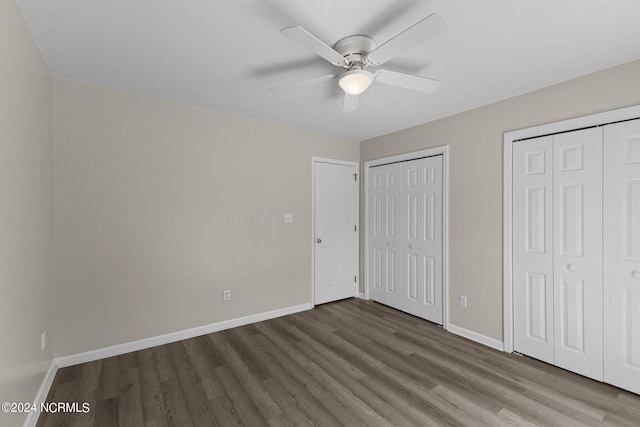 unfurnished bedroom featuring ceiling fan, dark wood-type flooring, and two closets