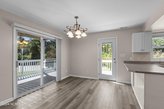 unfurnished dining area featuring a chandelier, light wood-type flooring, and a healthy amount of sunlight