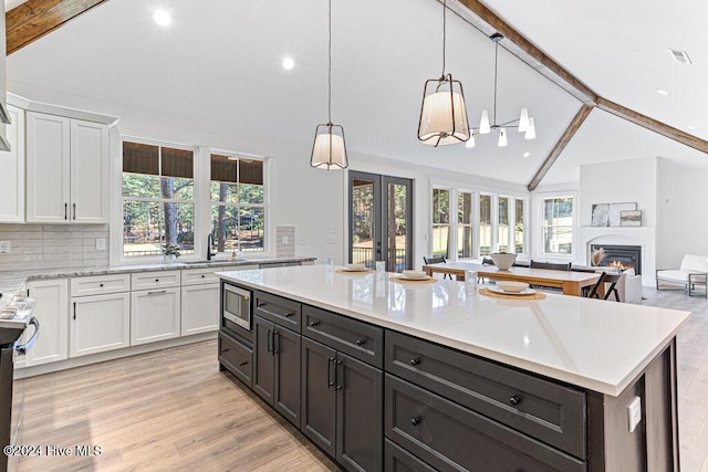 kitchen with stainless steel microwave, plenty of natural light, white cabinets, and light hardwood / wood-style flooring