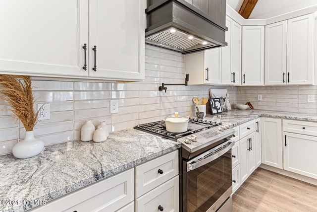 kitchen with gas stove, light stone countertops, white cabinets, custom exhaust hood, and light wood-type flooring