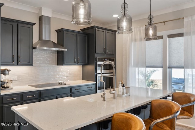 kitchen with pendant lighting, wall chimney range hood, a kitchen island with sink, double oven, and black electric cooktop