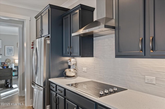 kitchen with wall chimney exhaust hood, stovetop, tasteful backsplash, stainless steel refrigerator, and light stone countertops