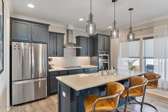 kitchen with wall chimney exhaust hood, decorative light fixtures, appliances with stainless steel finishes, a kitchen breakfast bar, and an island with sink