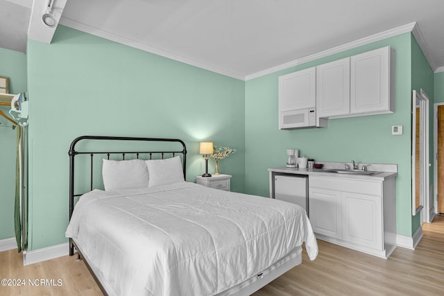 bedroom with light wood-style floors, crown molding, baseboards, and a sink