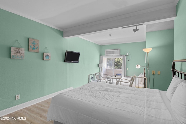 bedroom with an AC wall unit, ornamental molding, wood finished floors, and baseboards