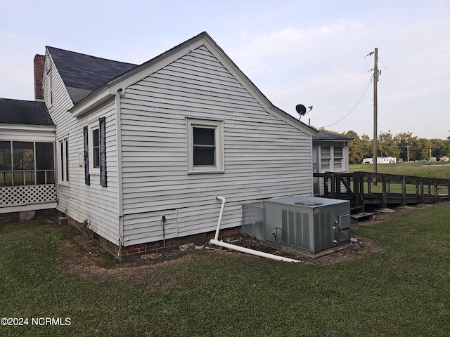 view of side of home featuring central AC unit, a lawn, a chimney, and a sunroom