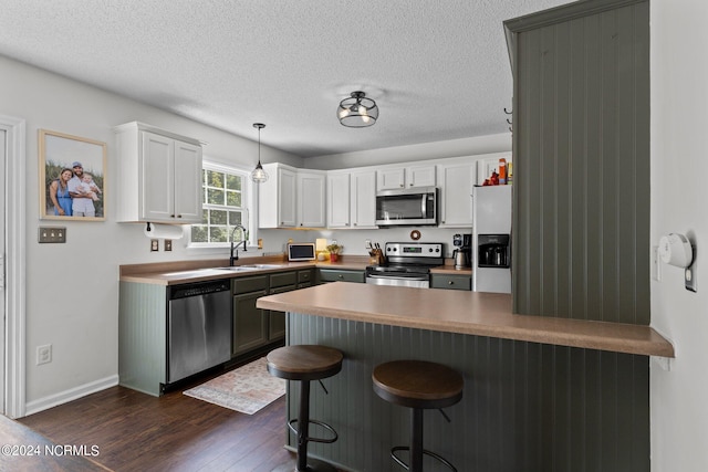 kitchen with white cabinetry, dark wood-type flooring, stainless steel appliances, kitchen peninsula, and decorative light fixtures