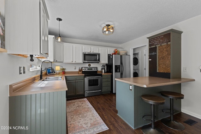 kitchen with stainless steel appliances, dark hardwood / wood-style flooring, kitchen peninsula, stacked washer and dryer, and decorative light fixtures