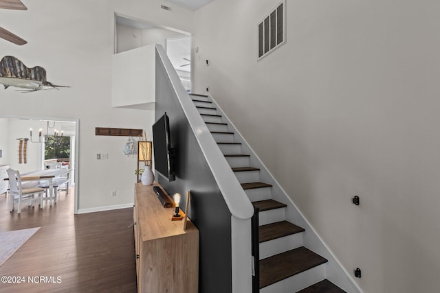 stairs with a high ceiling, ceiling fan with notable chandelier, and hardwood / wood-style flooring