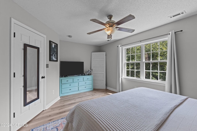 bedroom with ceiling fan, light hardwood / wood-style floors, and a textured ceiling