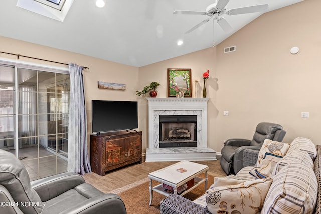 living room featuring wood finished floors, a high end fireplace, visible vents, a ceiling fan, and lofted ceiling with skylight