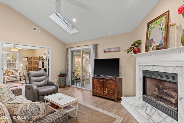 living area featuring a fireplace, visible vents, a ceiling fan, lofted ceiling with skylight, and wood finished floors