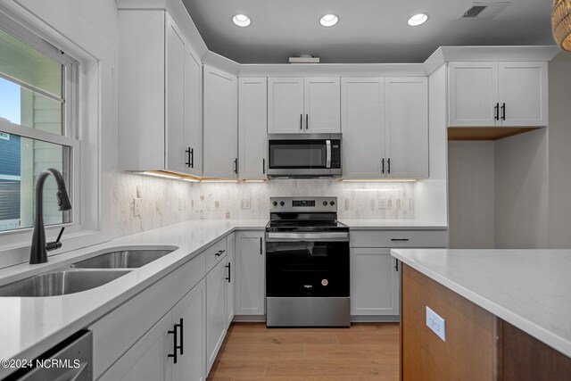 kitchen with appliances with stainless steel finishes, white cabinetry, light stone countertops, light wood-type flooring, and sink