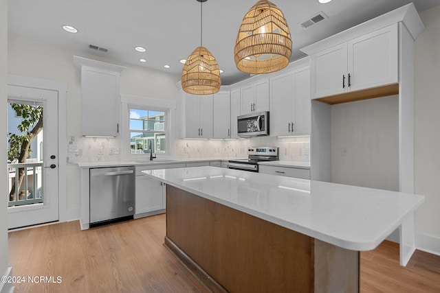 kitchen with white cabinetry, a kitchen island, pendant lighting, stainless steel appliances, and light wood-type flooring