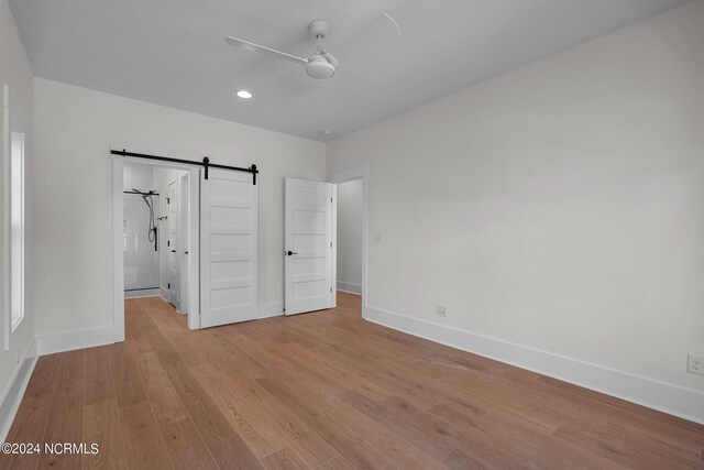 unfurnished bedroom with light hardwood / wood-style flooring, ceiling fan, and a barn door