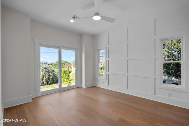 empty room featuring ceiling fan, light wood-style flooring, visible vents, and a decorative wall