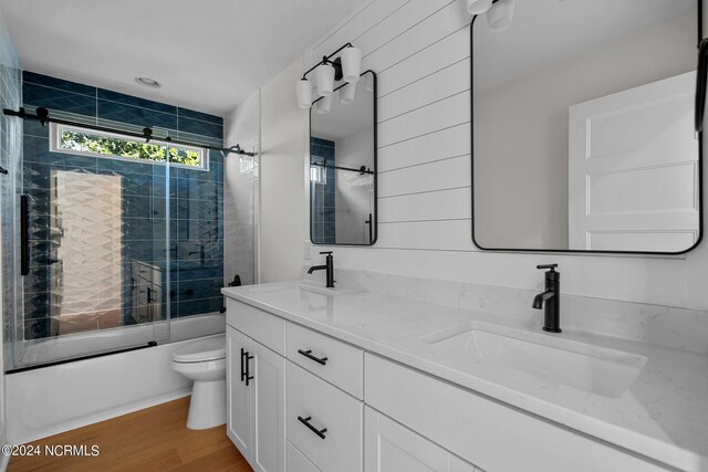 full bathroom with bath / shower combo with glass door, hardwood / wood-style flooring, vanity, and toilet