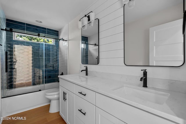 bathroom featuring double vanity, toilet, wood finished floors, combined bath / shower with glass door, and a sink