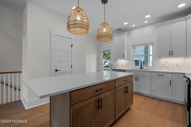 kitchen featuring tasteful backsplash, sink, white cabinets, hanging light fixtures, and light hardwood / wood-style flooring