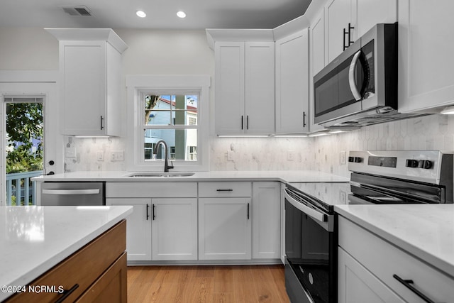 kitchen with appliances with stainless steel finishes, white cabinetry, tasteful backsplash, light hardwood / wood-style flooring, and sink