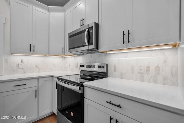 kitchen with stainless steel appliances, white cabinetry, light wood-type flooring, and backsplash