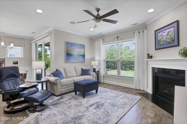 living room with light wood-type flooring, ceiling fan with notable chandelier, and ornamental molding