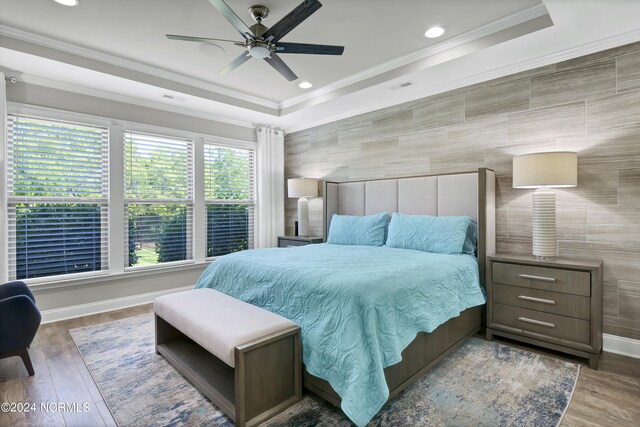 bedroom featuring tile walls, ceiling fan, a raised ceiling, and wood-type flooring