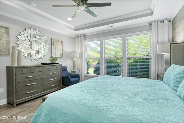 bedroom with crown molding, ceiling fan, a tray ceiling, and light hardwood / wood-style floors