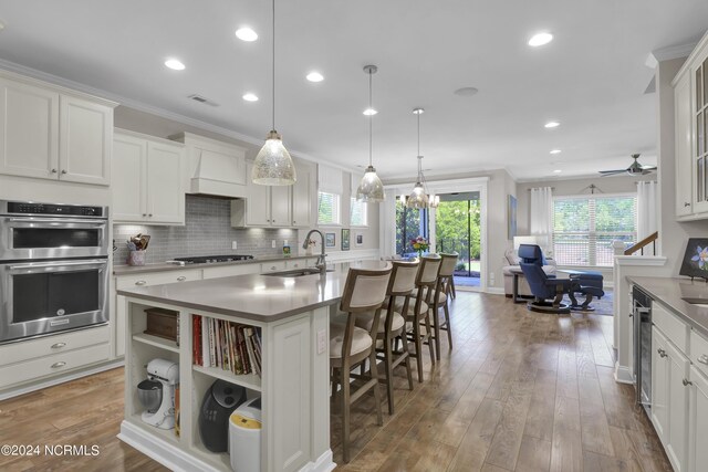 kitchen with light wood-type flooring, ceiling fan with notable chandelier, stainless steel appliances, a kitchen bar, and a kitchen island with sink