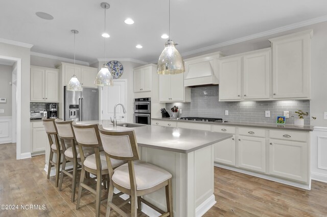 kitchen with a kitchen island with sink, custom range hood, light hardwood / wood-style flooring, and stainless steel appliances