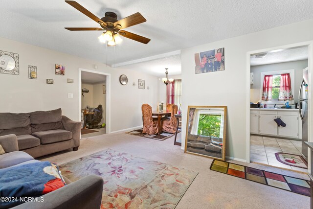 living area with a ceiling fan, light carpet, a textured ceiling, and baseboards