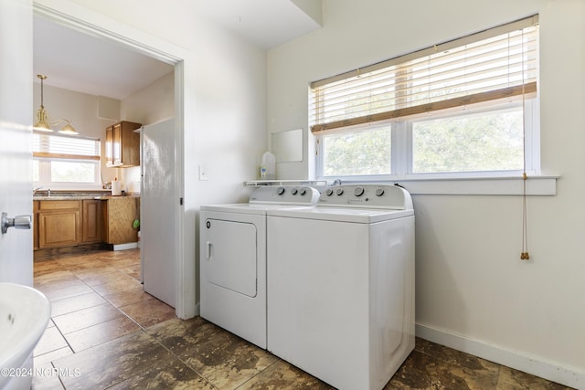 clothes washing area featuring laundry area, stone finish floor, washer and clothes dryer, and baseboards