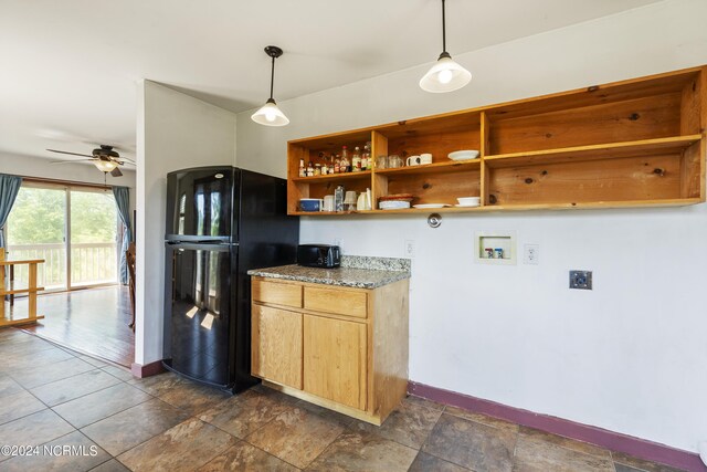 kitchen featuring light stone counters, black fridge, hanging light fixtures, and ceiling fan